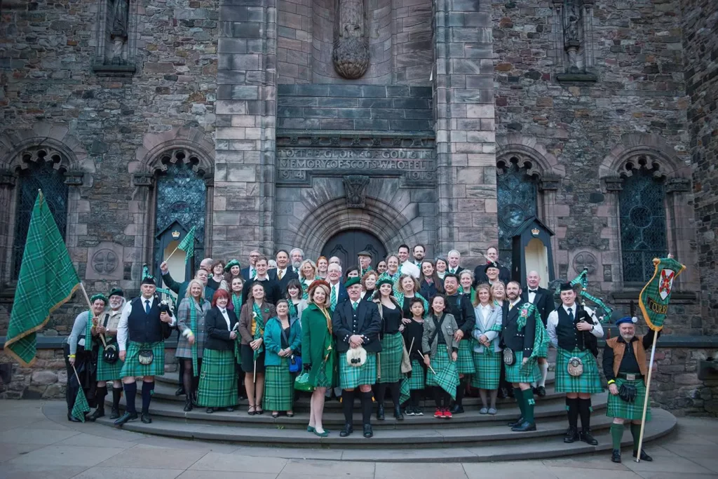 a group people standing in front of an stone church wearing varying types of Learned Kindred of Curie Tartan